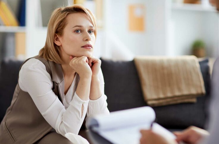 Young serious and concentrted woman listening to her counselor while sitting on couch during consultation