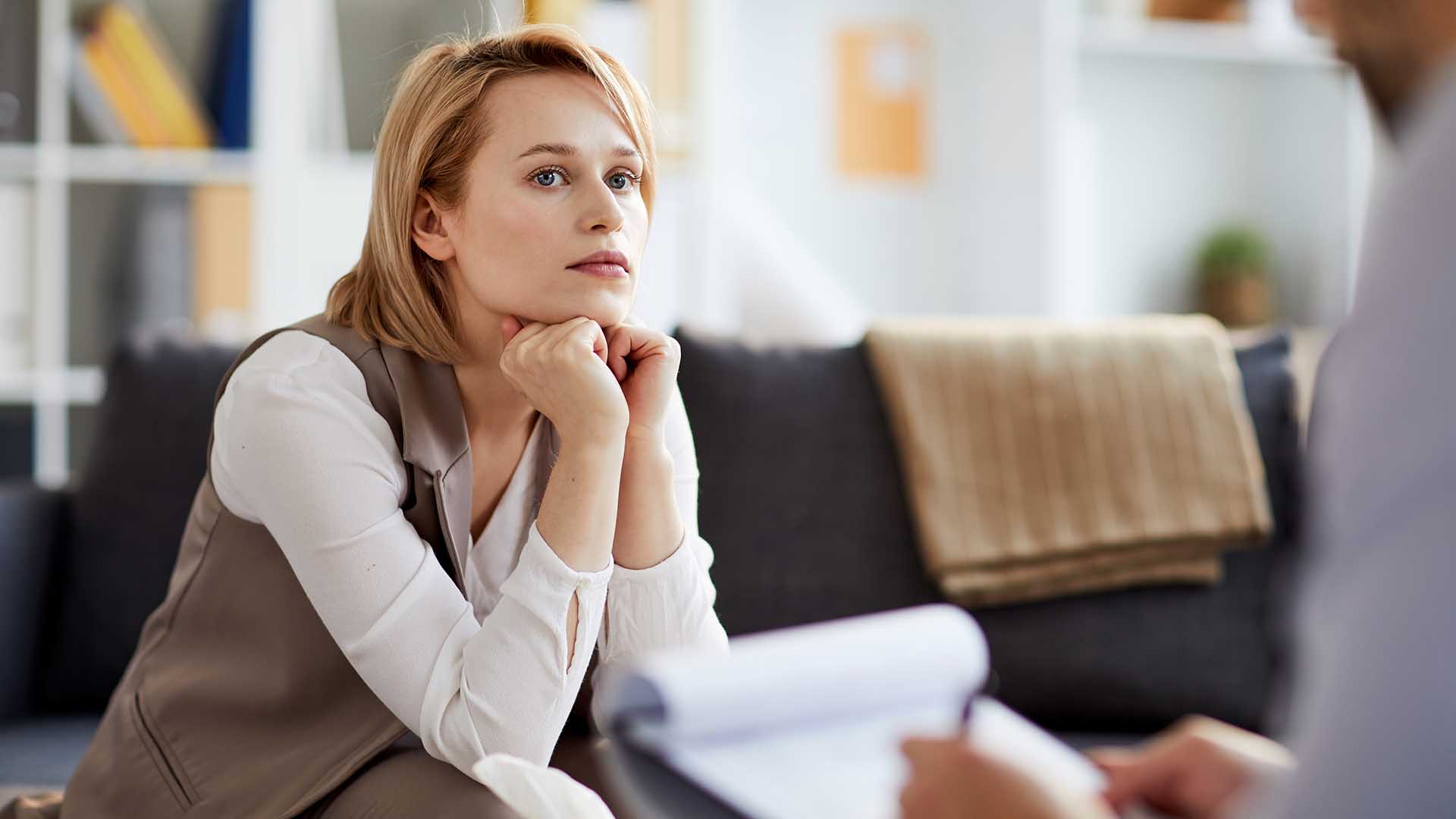 Young serious and concentrted woman listening to her counselor while sitting on couch during consultation